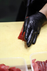 mano con guantes de un experto en sushi cortando atún rojo para elaborar sushi