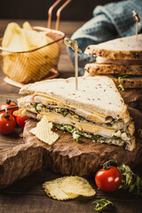 Stacked sandwich featuring fresh ingredients, served on a wooden board with crispy chips and cherry tomatoes, highlighting a delightful culinary experience