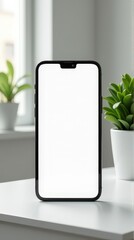 Modern smartphone with blank screen on white desk near window and green plants.