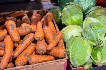 Fresh organic vegetables carrots and green cabbages displayed in a rustic wooden crate at a vibrant local farmers market showcasing healthy produce options