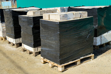 Stacked pallets of wrapped white stone blocks in a construction yard, showcasing organized materials ready for building projects and landscaping applications.