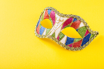 Vibrant image of a colorful masquerade mask adorned with intricate designs, placed against a bright yellow background. The mask is decorated with glittering patterns. Copy space.