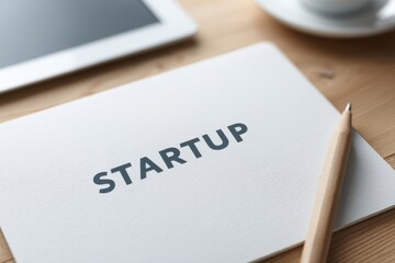 A notebook labeled "STARTUP" next to a pencil and tablet on a wooden desk, symbolizing new business ideas and entrepreneurship.