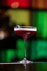 purple cocktail with a foamy white top is garnished with skewered blueberries on a textured bar surface