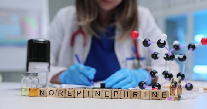 Word Norepinephrine on wooden blocks near molecular model against scientist at work. Woman doctor analyzes materials structure in medical lab