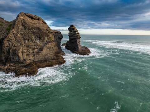 Coastal view of the Tasman sea, with rocky cliffs and sea stacks. Waves crash against the rocks, creating a dynamic scene. PIHA, NZ
