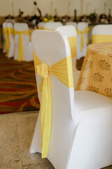 Elegant wedding reception chair and table setting. White chair cover accented with yellow sash. Festive event decor with sunny color scheme.