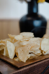 Crispy papadams sit piled on a wooden tray, the delicate snacks an invitation to savory flavors, backgrounded by a decorative vase.