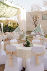 Elegant outdoor event with draped seating, floral centerpieces, and stylish decor creates a festive...