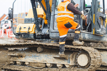 Construction worker  in bright safety gear working hard using shovel to clean tracks of his heavy...