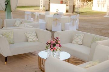 Outdoor event lounge area with white couches, decorative pillows, and floral centerpiece on a round...