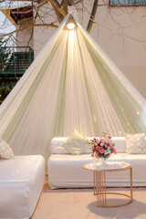 Outdoor lounge area with draped fabric, soft cushions, and a floral centerpiece. Ideal for relaxation or intimate gatherings.