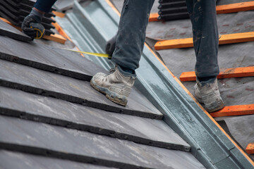 Builder carefully places roof tiles on a sloped surface while standing on top of a building showcasing the effort involved in roofing work