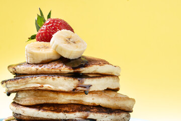Pancakes with chocolate and fruit on yellow background. Close up