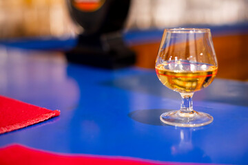 Single Whisky Glass with Golden Scotch on Blue Bar Counter – Horizontal Composition of Elegant Drink in Snifter, Warm Bar Ambience and Nightlife Atmosphere