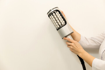 Close-up of a hand holding a modern anti-cellulite massage device used in professional cosmetic...