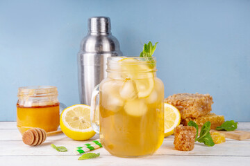 Citrus and honey cocktail, iced sweet tea or mead lemonade in glass mason jar,  with honey mead strong liqueur, lemon juice and mint decor, on white table with honeycomb, honey jar and dipper