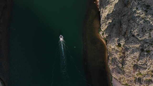 Aerial view of a boat cruising through the Zrmanja river canyon in Croatia, surrounded by steep cliffs and crystal-clear green water. Ideal for nature, travel, and adventure visuals.