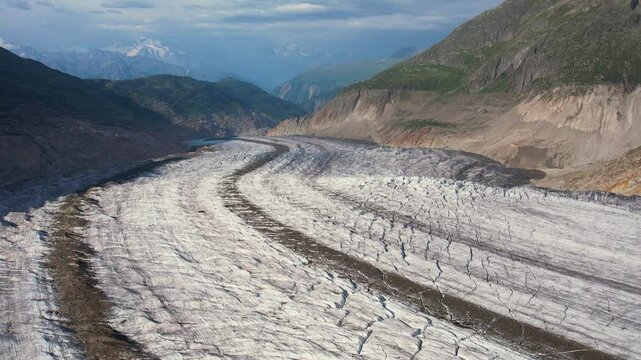 Aerial drone view of stunning view of the Aletsch Glacier in the Swiss Alps, showcasing the immense ice flow surrounded by towering mountains under a clear blue sky. Highlights nature's grandeur.
