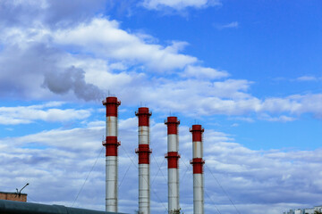 Four red and white industrial pipes stand out against a clear blue sky filled with clouds
