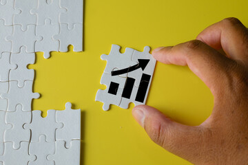 Concept of business growth and improvement, with a hand placing a puzzle piece featuring an upward arrow, symbolizing success, progress, and the path to achieving goals.
