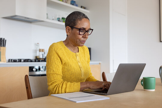 Mature woman working on Laptop in Modern Kitchen Setting