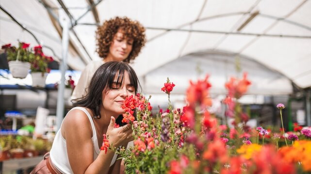 Woman smelling colorful flowers in greenhouse with friend