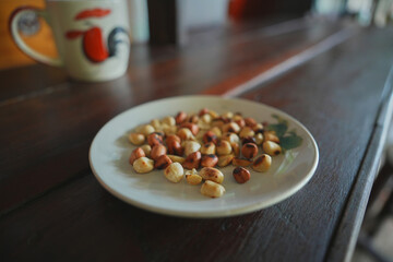 Roasted peanuts with salt in a plate placed on a wooden table.