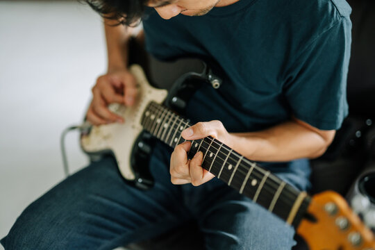 An individual in relaxed setting passionately strums the strings of a guitar, immersed in the music's creation. Capturing the essence of artistry and creative passion.