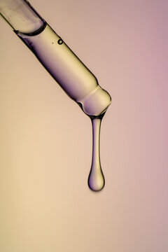 Close-up of a dropper with serum against colored background