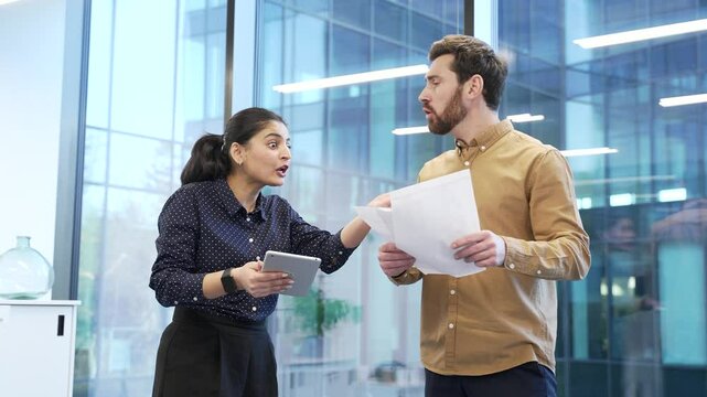 Two angry co-workers, a man and a woman arguing intensely in a modern office setting, showcasing conflict and emotion during heated business discussion or disagreement. Colleagues arguing, quarreling