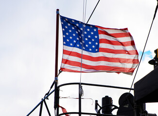 American Flag Flying Above Ship Equipment. The United States flag flutters atop a ship against a...