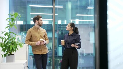 Two colleagues engaged in friendly conversation with coffee in modern office setting. Co-workers, a man and a woman have a friendly conversation. Teamwork, effective communication and collaboration - Powered by Adobe