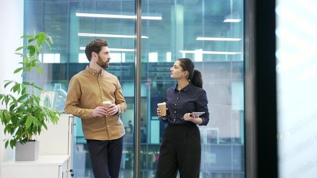 Two colleagues engaged in friendly conversation with coffee in modern office setting. Co-workers, a man and a woman have a friendly conversation. Teamwork, effective communication and collaboration - Powered by Adobe