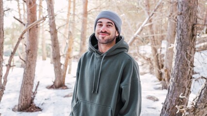 Young man smiling in snowy forest wearing hoodie and beanie
