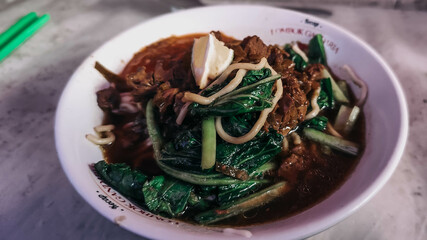 A bowl of chicken noodles with vegetables and chili sauce