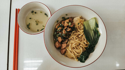 a bowl of noodles with chicken and vegetables served with separate broth