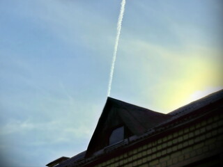 thin plane trail in blue sky above triangular roof, geometric shape in sunlight