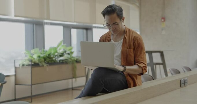 Senior Asian businessman wearing headset celebrates success during online meeting in modern co-working space. Remote work and business communication concept.