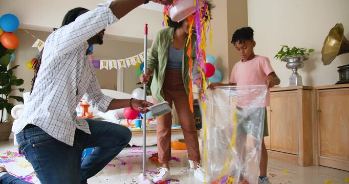 Happy black couple and multiracial son tidying and cleaning living room after celebrating boy's birt