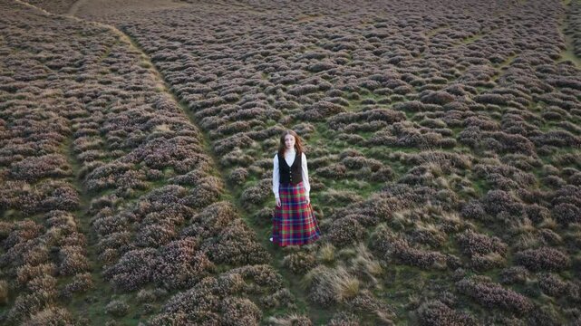 Woman in tartan skirt standing in vast heather field during autumn

