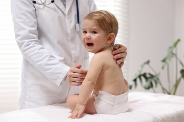 Pediatrician examining cute little crying baby in clinic, closeup