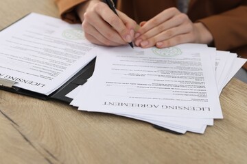 Obraz premium Woman signing licensing agreement document at wooden table indoors, closeup