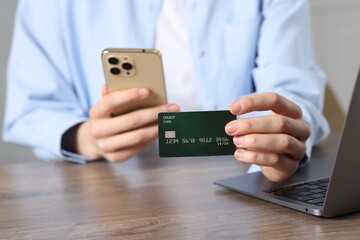 Woman with credit card, smartphone and laptop paying online at wooden table, selective focus