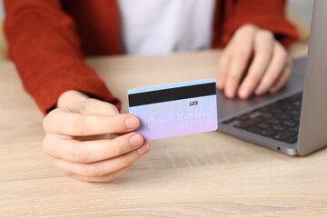 Online payment. Woman with credit card and laptop at wooden table, closeup
