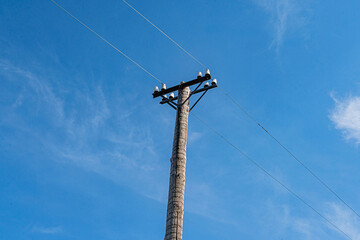 Utility pole against a clear blue sky, multiple crossarms, power lines at varying heights, rural or...