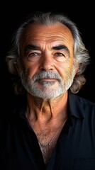 Close-up portrait of an older man with gray hair and a beard, wearing a black shirt against a dark background, showcasing wisdom and experience.