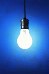 Glowing light bulb hanging against blue textured wall in studio shot vertical composition