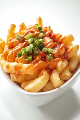Close up of delicious french fries topped with spicy sauce and green onions in a white bowl on a white background