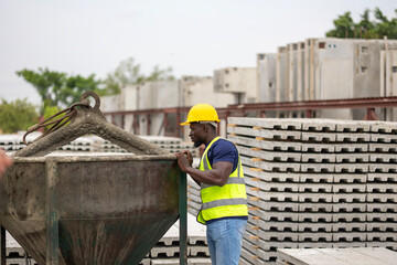 Female worker or engineer wearing safety gear, a yellow hard hat and vest. Construction worker is holding a clipboard standing near a large concrete bucket as part of an active construction operation.